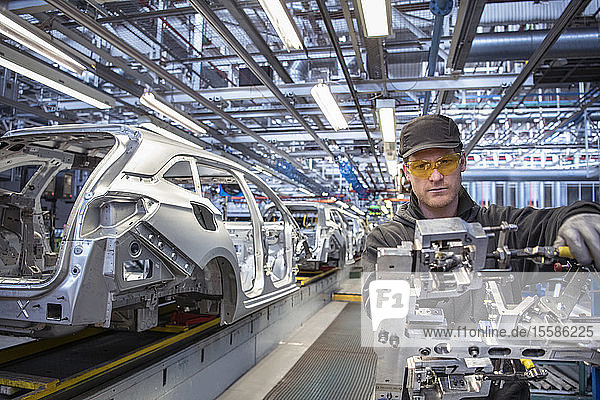 Car worker fitting parts on production line in car factory