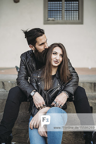Mann küsst Haare und umarmt Frau von hinten auf Stufen