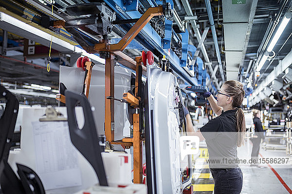 Female worker assembling car doors on production line in a car factory