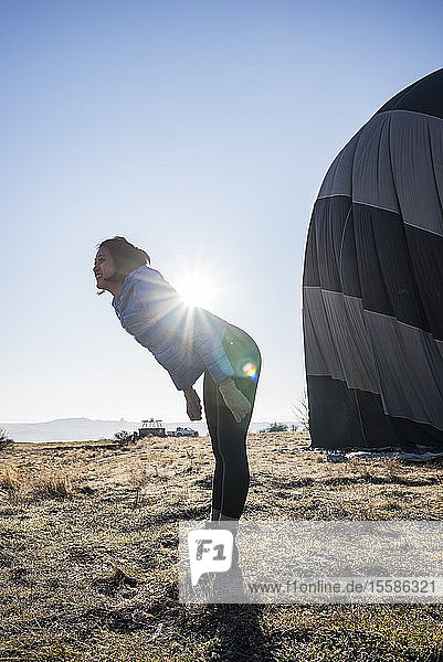 Woman bending forward against sunlight  hot air balloon in background  GÃ¶reme  Cappadocia  Nevsehir  Turkey
