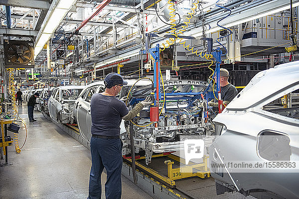 Autoarbeiter montieren Motorhauben an Autos am Fließband in einer Autofabrik