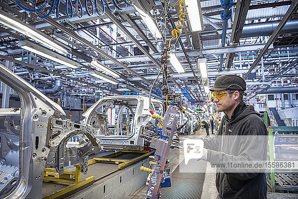 Car worker fitting parts on production line in car factory