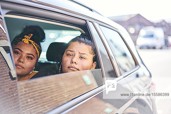 Two teenage girls in car back seat looking out of car window