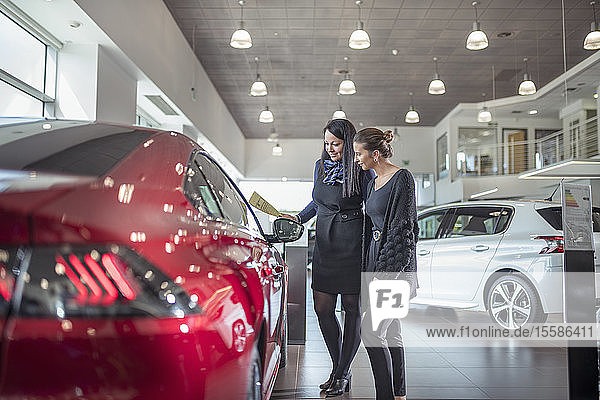 Saleswoman and customer inspecting new car in car showroom