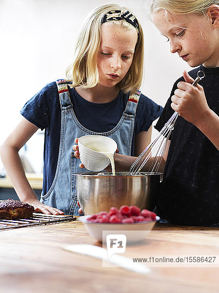 Mädchen und ihre Schwester backen einen Kuchen und gießen Sahne in eine Rührschüssel am Küchentisch