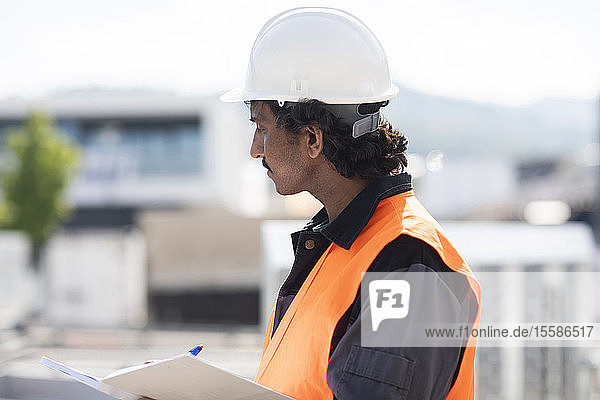 Männlicher Ingenieur vor einem Industriegebäude beim Schreiben in ein Notizbuch  Seitenansicht