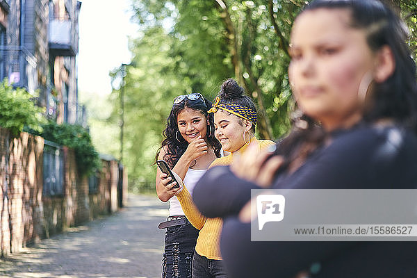 Young woman with teenage sisters looking at smartphone by park