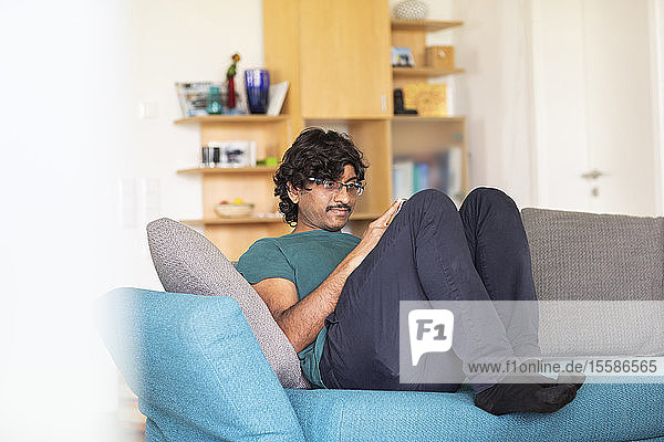 Mittelgroßer Mann entspannt sich auf dem Sofa und schaut auf ein Smartphone