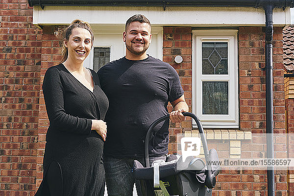 Couple carrying baby in cradle in front of house