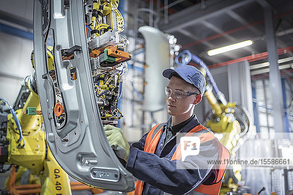 Auszubildender Ingenieur beim Justieren eines Roboters in einer Autofabrik