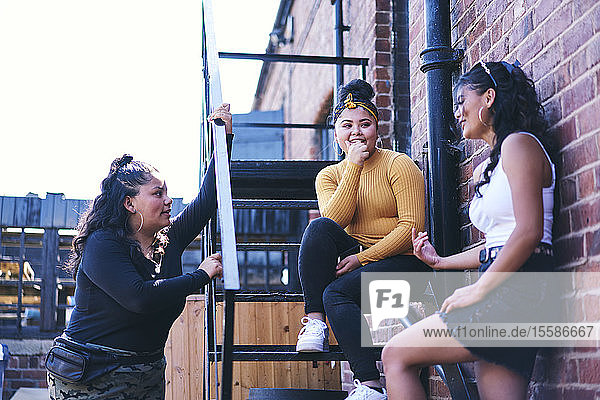 Young woman and her teenage sisters chatting on fire escape