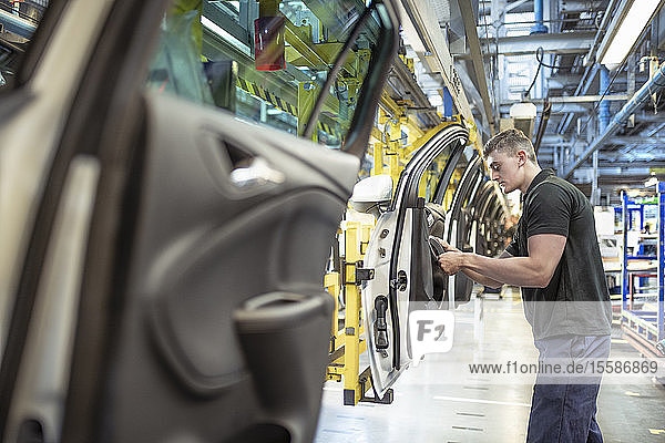 Male apprentice engineer assembling car doors in car factory