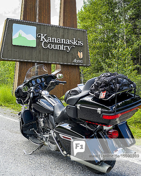 A motorcycle parked on the roadside of Bighorn Highway (Highway 40) in front of a sign for Kananaskis Country Peter Lougheed Provincial Park; Alberta Canada