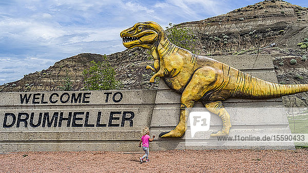 Large sign 'Welcome to Drumheller' with dinosaur and young girl running towards it; Drumheller Alberta Canada