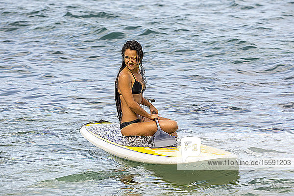 Girl sitting on stand up paddle board; Maui  Hawaii  United States of America