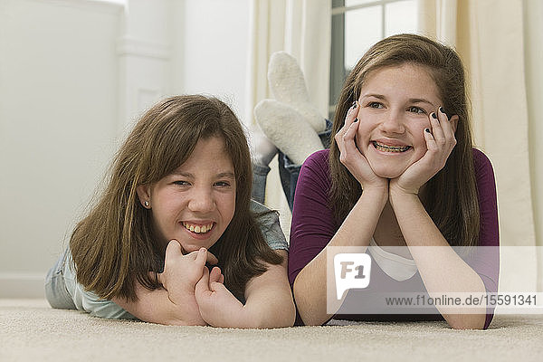 Zwei Teenager-Mädchen liegen zusammen und lächeln  Teenager-Mädchen mit Geburtsfehler im Gespräch mit einem Mobiltelefon