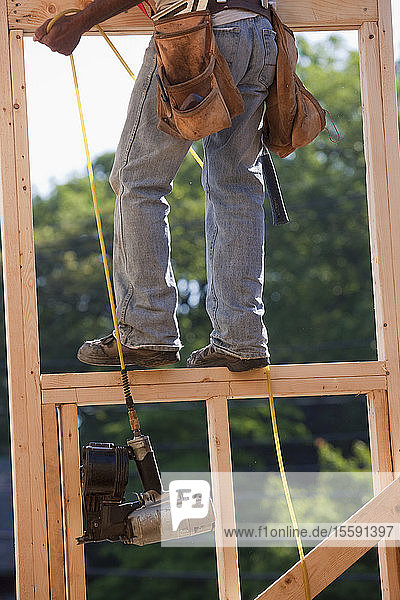 Zimmermann beim Hochziehen der Nagelpistole in den zweiten Stock eines im Bau befindlichen Hauses