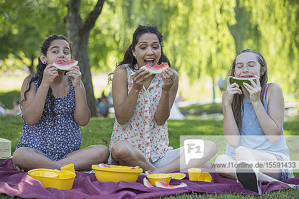 Glückliche hispanische Familie beim Picknick und beim Verzehr von Wassermelonen in einem Park