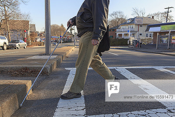Ein Mann mit angeborener Blindheit überquert die Straße mit seinem Blindenstock