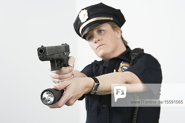 Police woman pointing handgun and holding flashlight.