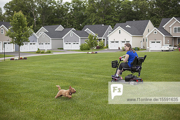 Junge Frau mit zerebraler Lähmung fährt mit ihrem Motorroller auf ihrem Rasen