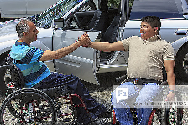 Freunde mit Rückenmarksverletzungen in Rollstühlen grüßen sich gegenseitig