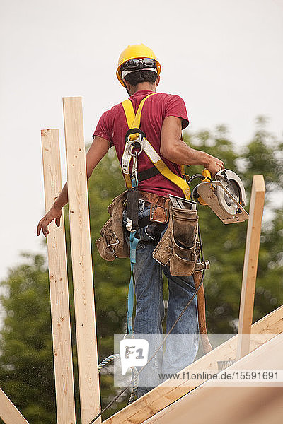 Hispanic carpenter using a circular saw on the roof at a house under construction