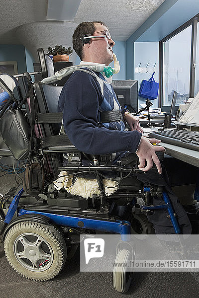 Geschäftsmann mit Duchenne-Muskeldystrophie in einem motorisierten Rollstuhl bei der Arbeit in einem Büro