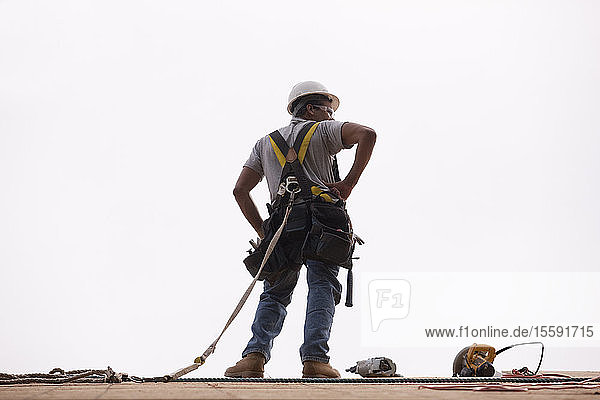 Ein hispanischer Zimmermann steht mit Hammer  Kreissäge und Nagelpistole auf dem Dach