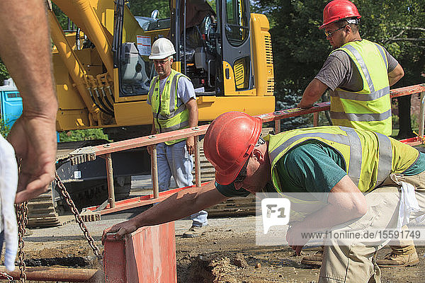 Bauarbeiter bereiten sich darauf vor  mit einer Leiter in ein Loch zu steigen