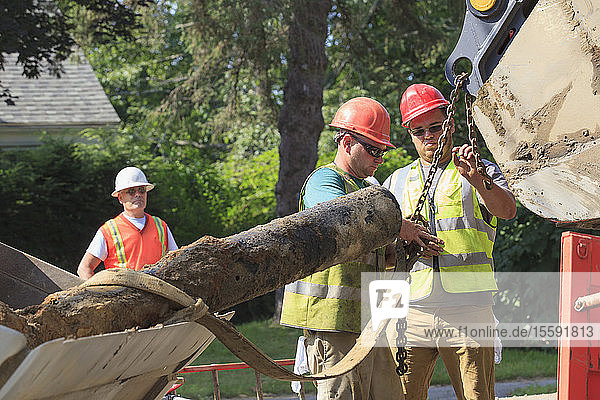 Bauarbeiter haken alte Wasserleitung vom Bagger ab