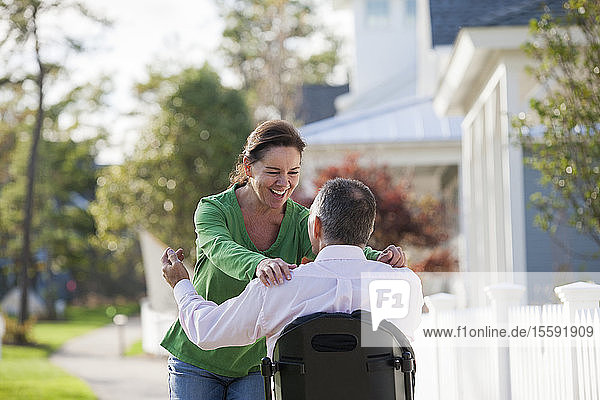 Ein Paar begrüßt sich glücklich  während er mit einer Rückenmarksverletzung im Rollstuhl sitzt