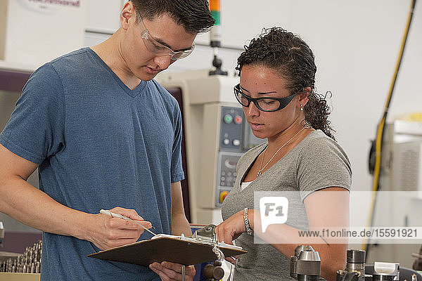 Engineering students reviewing notes on clipboard in a machine lab