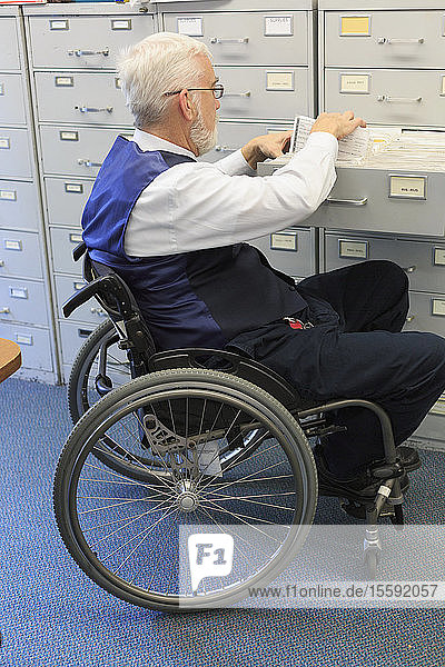 Mann mit Muskeldystrophie im Rollstuhl  der in einem Büro Dokumente zieht