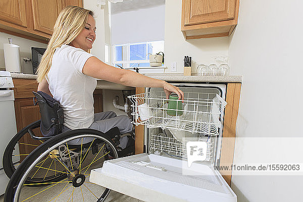 Frau mit Rückenmarksverletzung stellt in ihrer barrierefreien Küche eine Tasse in den Geschirrspüler
