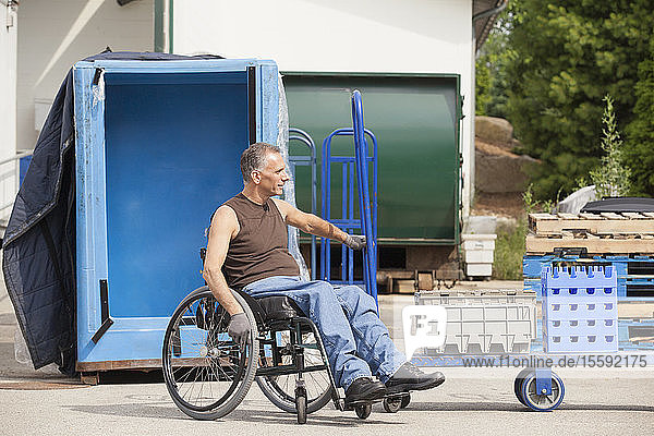 Laderampenarbeiter mit Rückenmarksverletzung im Rollstuhl beim Bewegen einer Sackkarre