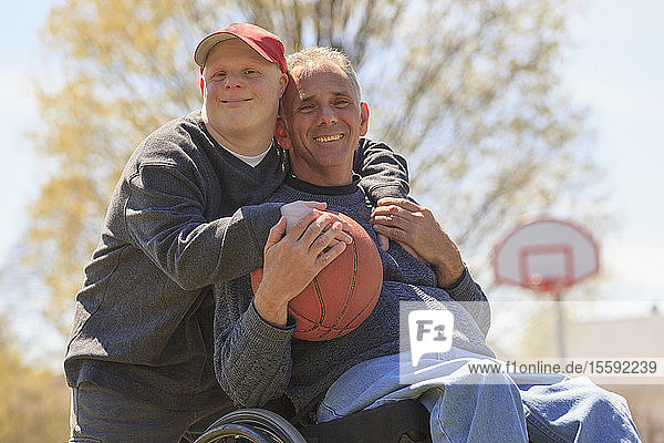 Portrait of happy father with Spinal Cord Injury and his son with Down Syndrome holding a basketball in park