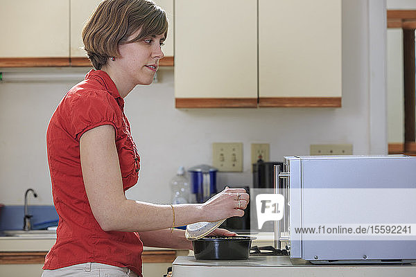 Junge blinde Frau kocht in ihrer Küche mit ihrer Mikrowelle