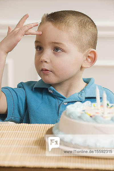 Junge  der vor einer Geburtstagstorte sitzend das Wort Sick in amerikanischer Zeichensprache gebärdet