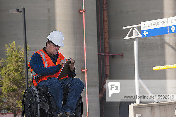Techniker im Rollstuhl bei der Inspektion von Lagertanks im Freien und der Aufzeichnung von Daten