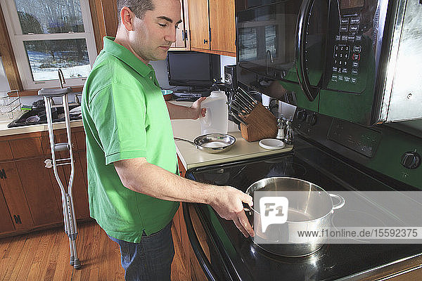 Mann nach Operation des vorderen Kreuzbandes (ACL) mit Krücken beim Kochen in der Küche