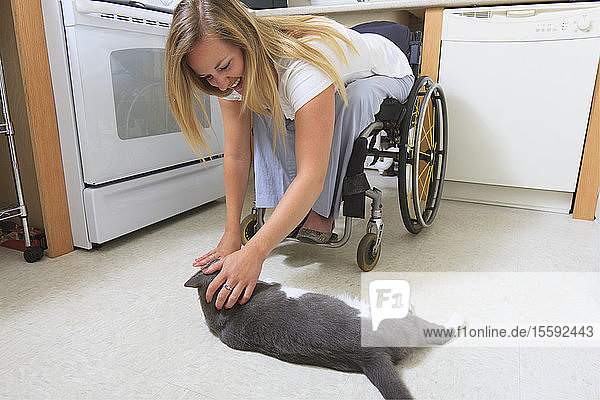 Frau mit Rückenmarksverletzung in ihrer barrierefreien Küche beim Spielen mit ihrer Katze