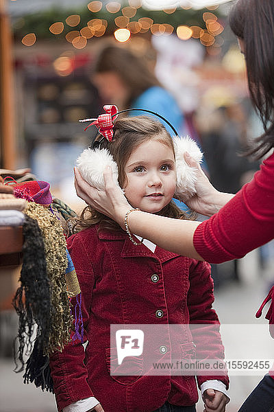 Frau probiert beim Weihnachtseinkauf Ohrenschützer an den Ohren ihrer Tochter an