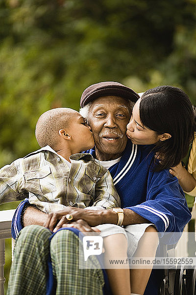 Ein älterer Mann  der im Rollstuhl sitzt  wird von seinem Enkel auf die Wange geküsst