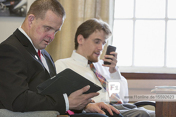 Man with Down Syndrome working as a Legislative Assistant using a tablet with his colleague on the phone in the State Capitol office