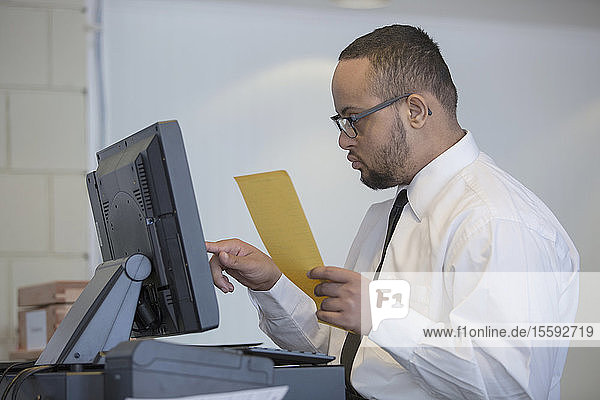 Afroamerikanischer Mann mit Down-Syndrom als Kellner  der einen Verkauf am Computer einträgt