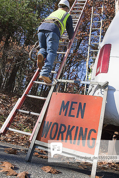 Kabelinstallateur klettert auf eine Leiter in der Nähe eines Men at Work-Schildes