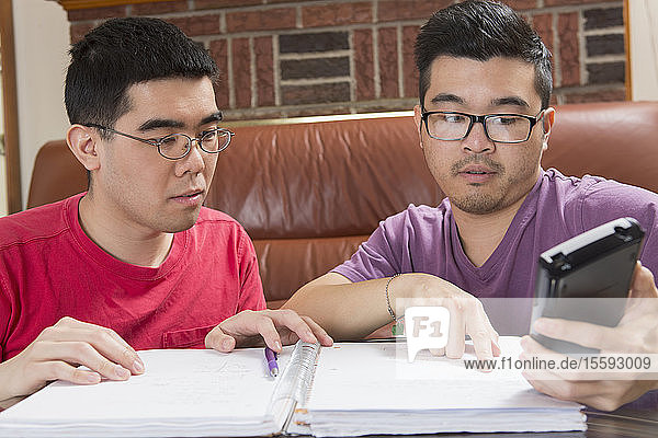 Asiatischer Mann mit Autismus arbeitet mit seinem Bruder am Telefon an seinen Hausaufgaben