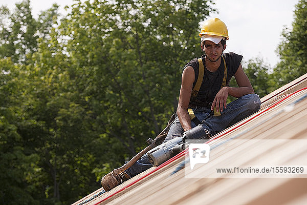Spanischer Zimmermann  der sich mit einer Nagelpistole auf der Dachkonstruktion eines Hauses ausruht