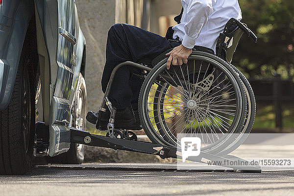 Geschäftsmann mit Muskeldystrophie im Rollstuhl beim Einsteigen in seinen behindertengerechten Lieferwagen auf dem Parkplatz